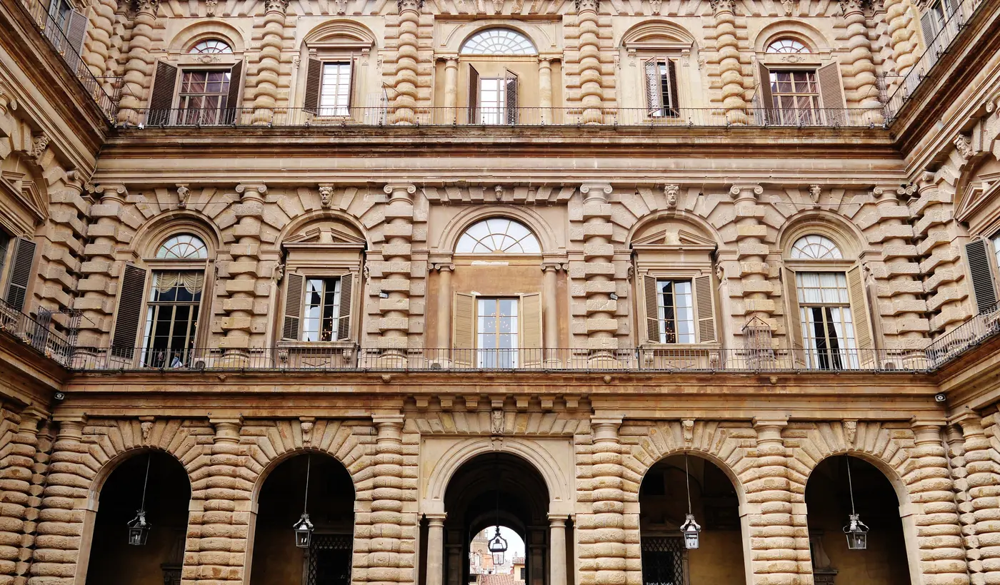 A stone courtyard of Palazzo Pitti in Florence, its heavy rough-cut walls pierced by arches and rows of windows