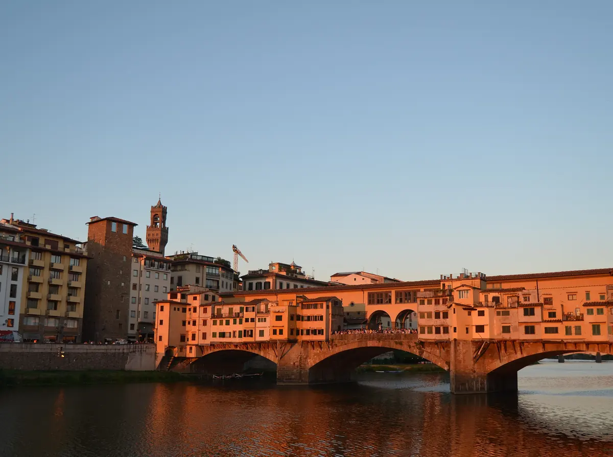 The Ponte Vecchio at sunset in Florence, with the shops on the bridge lit orange above the Arno