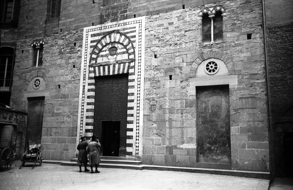 A black and white photograph of the striped marble portal of Santo Stefano al Ponte in Florence, with two people standing in the doorway